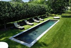 an outdoor swimming pool surrounded by grass and lawn furniture, with lounge chairs around it