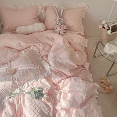 a bed with pink sheets and pillows in a room next to a table filled with stuffed animals