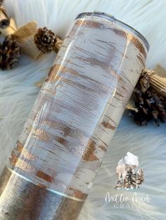 a gold and silver tumbler sitting on top of a white fur covered floor next to pine cones