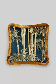 a blue and gold pillow with palm trees on the front, fringe trim around the edges