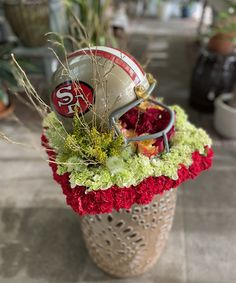 a football helmet sitting on top of a basket filled with red and green flowers in it