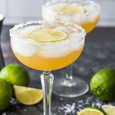 two margarita cocktails with lime and sugar garnish on the rim, surrounded by limes