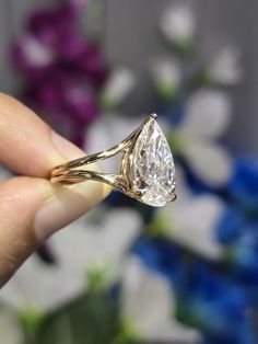 a person holding a ring with a diamond on it's finger and flowers in the background