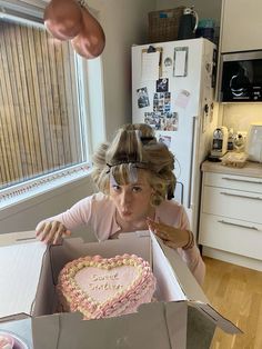 a woman holding a heart shaped cake in a box