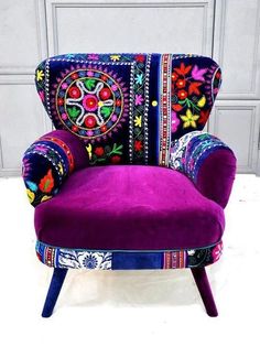 a purple chair with colorful embroidered designs on it's back and arms, sitting in front of a gray wall