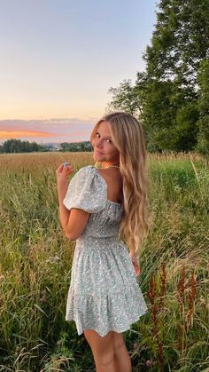 a woman standing in a field holding a toothbrush and looking at the camera while wearing a dress