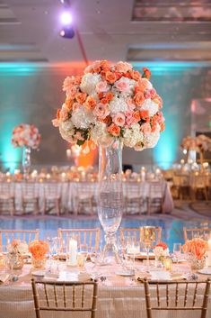 a tall vase filled with white and orange flowers on top of a table next to chairs