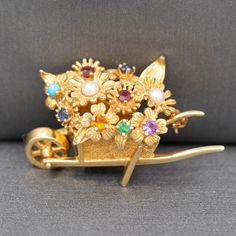 "Lovely Rare Dan Frere Gemstone Flowers in Wheelbarrow Brooch in Solid 14k Yellow Gold This absolutely darling playful piece by Dan Frere is rare and beautifully crafted as you would expect.  The brooch is in the shape of a wheelbarrow and features different floral forms, centered with real gemstones.  Garnet, pearl, turquoise, sapphire, emerald, citrine and amethyst.  The piece measures 1 3/8\" in length and is about 3/4\" in height.  It is crafted in 14k (stamped) and weighs 7.30g." Vintage Multi-stone Yellow Gold Brooches, Vintage Yellow Gold Multi-stone Brooches, Fine Jewelry Multi-stone Yellow Gold Brooches, Fine Jewelry Yellow Gold Multi-stone Brooches, Yellow Gold Multi-stone Brooches As Gift, Colombian Emeralds, Vintage Watches, Citrine, Antique Jewelry