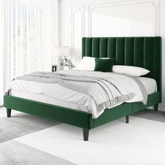 a bed with green headboard and pillows in a white room next to a window