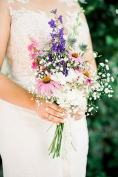 a woman holding a bouquet of flowers in her hands and wearing a wedding dress with lace on it