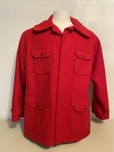 An MCM classic. Stand-out red wool in a classic longer ("car-coat") design with 8 pockets for the handy outdoorsman or woman. Button-front coat has a tan flannel lining with 6 front pockets (four with vintage logo buttons and two slip-in) plus two buttoned pockets in the side backs. Wrists have elasticized inner cuffs and outer flaps are adjustable by buttons to tighten against the weather. Label reads Woolrich Woolen Mills established 1830 Woolrich, Pa. 511 Size 46; fraying label still reads 10 Classic Solid Sport Coat With Pockets, Classic Solid Utility Jacket With Welt Pockets, Vintage Winter Utility Jacket With Lapel Collar, Vintage Utility Jacket With Lapel Collar For Winter, Solid Sport Coat With Pockets And Flat Front, Vintage Outerwear With Lapel Collar, Vintage Utility Jacket With Lapel Collar And Welt Pockets, Vintage Utility Jacket With Lapel Collar And Patch Pockets, Vintage Collared Outerwear In Solid Color