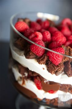 a layered dessert with raspberries and chocolate is displayed on a glass platter