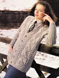 a woman leaning on a fence wearing a cabled sweater and jeans in the snow