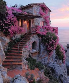 an old house with pink flowers growing on the side of it next to the ocean