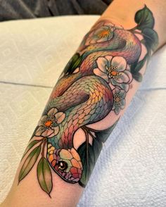 a woman's arm with a tattoo on it that has a snake and flowers on it