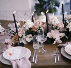 the table is set with white and pink flowers, silverware, and black candles