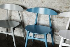 three different colored chairs sitting next to each other in front of a brick wall and cement floor