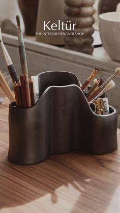 a pen holder with pens and pencils in it sitting on a wooden table next to a mirror