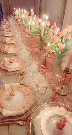 a long table is set with pink and white plates, silverware, and candles