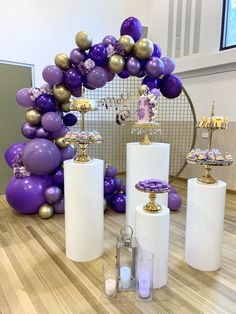 purple and gold balloons are on display in front of a white table with silver candles