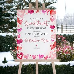 a baby shower sign in the snow with hearts on it's back and pink flowers behind it