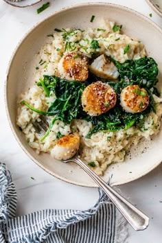 a white bowl filled with rice and scallops on top of a table next to silverware