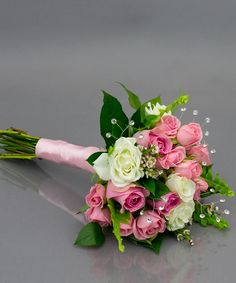 a bouquet of pink and white flowers on a gray surface with green leaves in the foreground