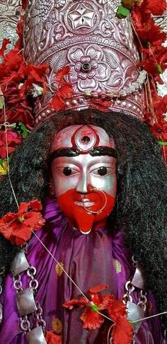 a person wearing a red and white mask with flowers around their neck, standing in front of a wall