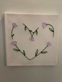 a heart made out of flowers on a white canvas with green stems in the shape of a flower