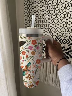 a person holding a coffee cup in front of a wall with flowers and butterflies on it