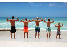 four men standing in front of the ocean flexing their muscles