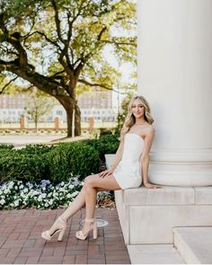 a beautiful young woman sitting on top of a white pillar