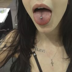 a woman sticking her tongue out with a cross on it's chest and piercings around her neck