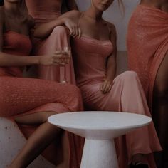 three women in pink dresses sitting next to each other on a white table and chair