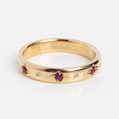 a yellow gold ring with three small diamonds on the side and two red stones in the middle