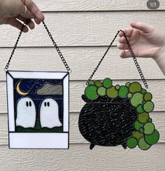 two handmade stained glass hangings with ghost faces on them, one is holding a black pot and the other has green leaves