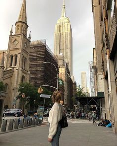 a woman walking down the street in front of tall buildings with spires on top