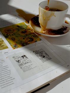 a cup of coffee sitting on top of a white table next to an open book