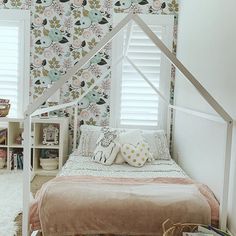 a white bed sitting under a window next to a wall covered in floral wallpaper