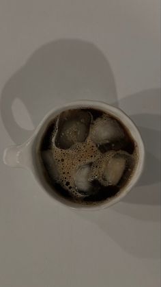 a cup filled with ice sitting on top of a white table next to a spoon