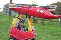 a child in a toy car with a kayak attached to the roof and seat