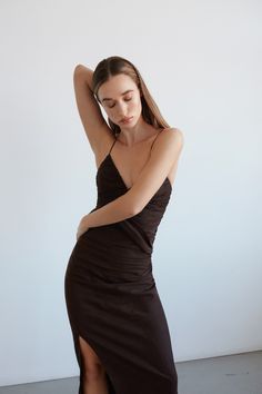 a woman in a black dress leaning against a wall with her hand on her head