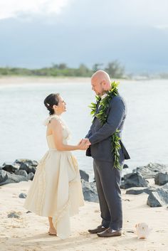 a bride and groom holding hands on the beach