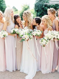 a group of women standing next to each other wearing dresses and holding bouquets in their hands