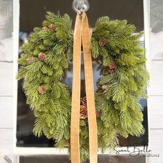 a green wreath with pine cones hanging on a window