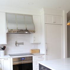 a kitchen with white cabinets and stainless steel range hood over the stove, in front of an oven