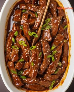 beef with sesame seeds and sauce in a white bowl on a black table top, with chopsticks