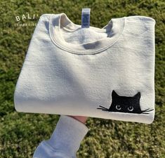 Snuggle up in style with our irresistibly adorable Cat Embroidered Sweatshirt! This cozy and charming sweatshirt features a delightful Cat Peeking design, making it the perfect wardrobe addition for any cat lover or proud cat mom/parent. HOW TO ORDER To place an order, follow these simple steps: 1. Select the size that fits you perfectly. 2. Choose your desired sweatshirt color from our selection of options. 3. Enter the thread color for the embroidery SIZING Please refer to the size chart provided in the product photos for accurate sizing. Our sweatshirts have a unisex fit, but if you prefer an oversized look, we recommend sizing up. PROCESSING TIME Once your order is placed, we'll get to work embroidering your sweatshirt with care. We strive to ship it out in 1 -3 business days using the Black Cat Clothes, Cute Cotton Sweatshirt With Cat Design, Long Sleeve Cotton T-shirt With Cat Design, Black Cotton Sweatshirt With Cat Design, Cotton Crew Neck Sweatshirt With Cat Design, Cat Embroidery Simple, Embroidery For Mom, Black Cat Embroidery, Cat Peeking