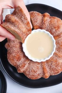 someone is dipping something into a small bowl on a black plate with powdered sugar