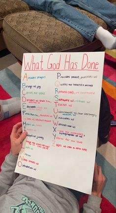 a young child holding up a sign that says what god has done on it while laying on the floor